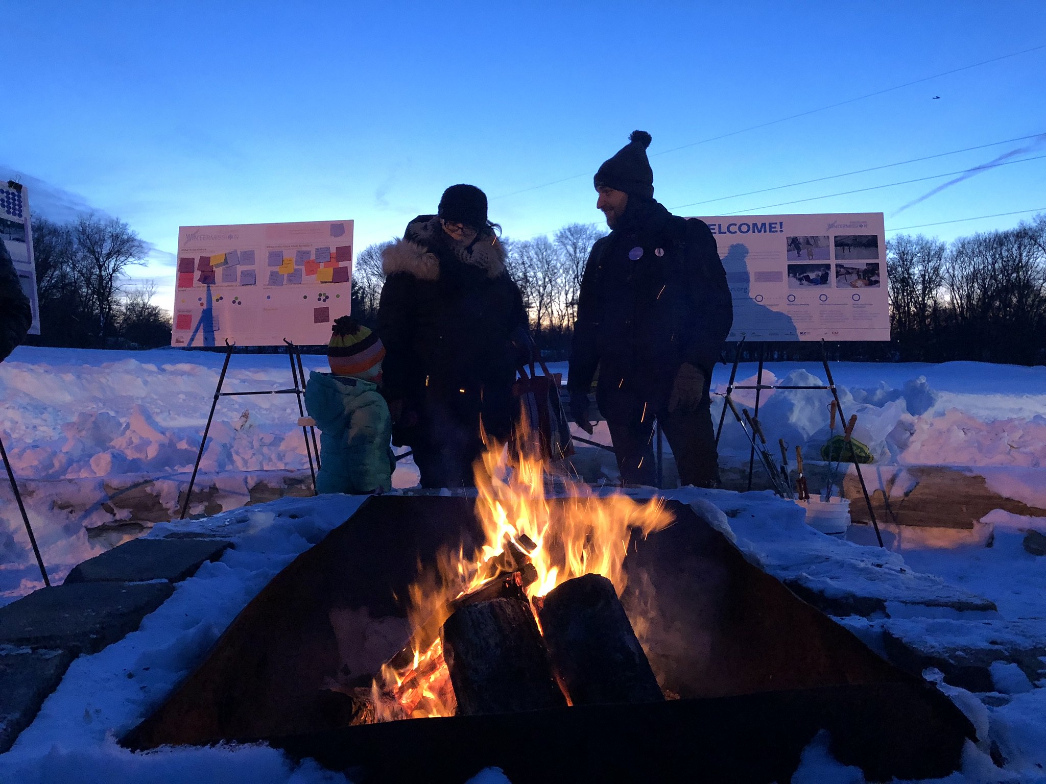 Two adults and a child enjoying an outdoor fire in a snowy location